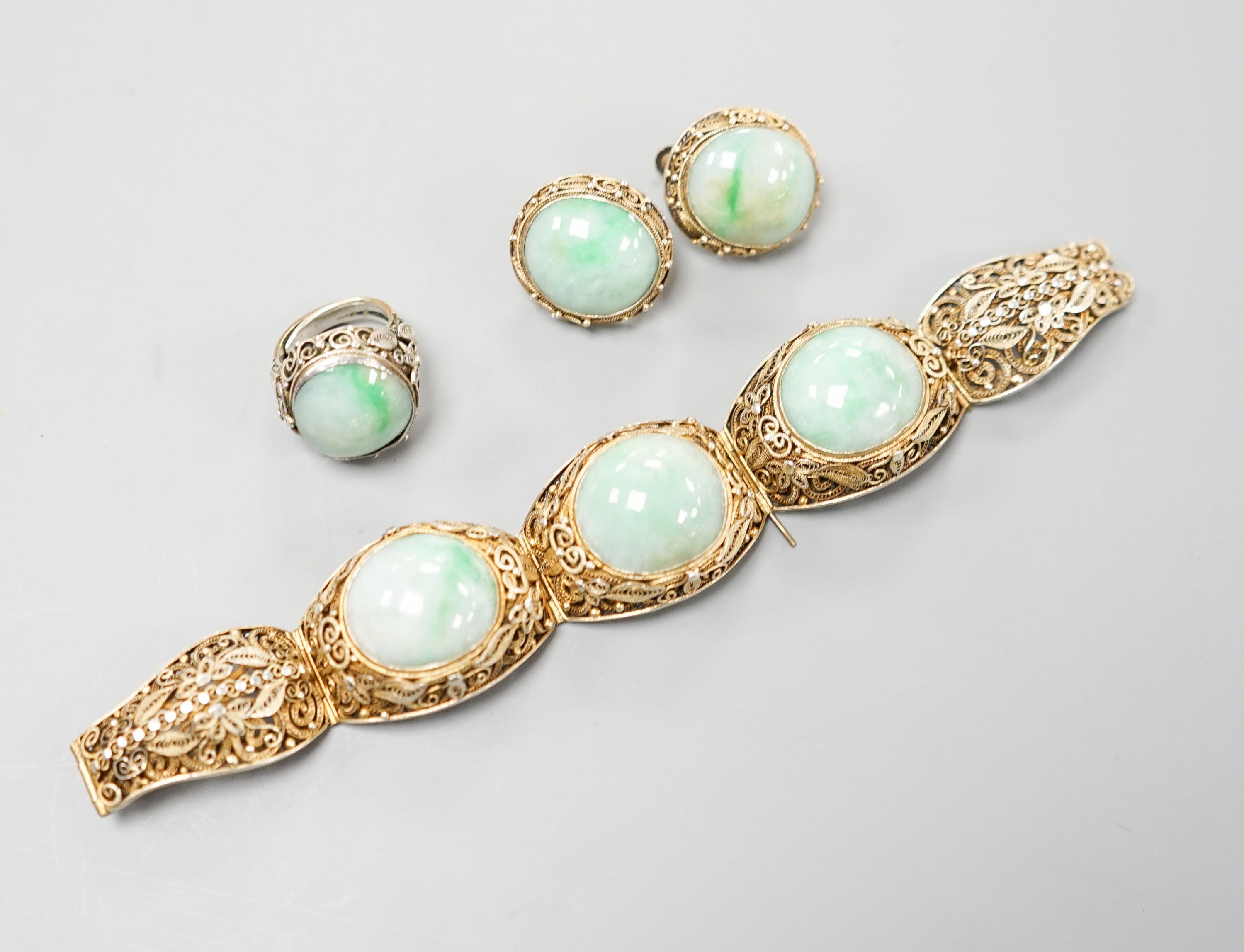 A Chinese filigree gilt white metal and three stone cabochon jade set bracelet, 17cm, a pair of matching ear clips, length 25mm and a similar white metal and cabochon jade set ring, size L.
